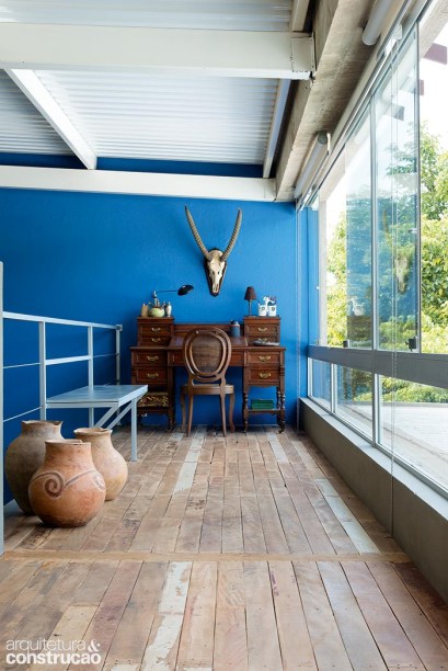 Um canto de trabalho com vista para a piscina ocupa este lado do mezanino. Aqui, como no restante do andar, o piso mudou para madeira de demolição. Este ângulo também evidencia a face interna das telhas termoacústicas (Ananda Metais).