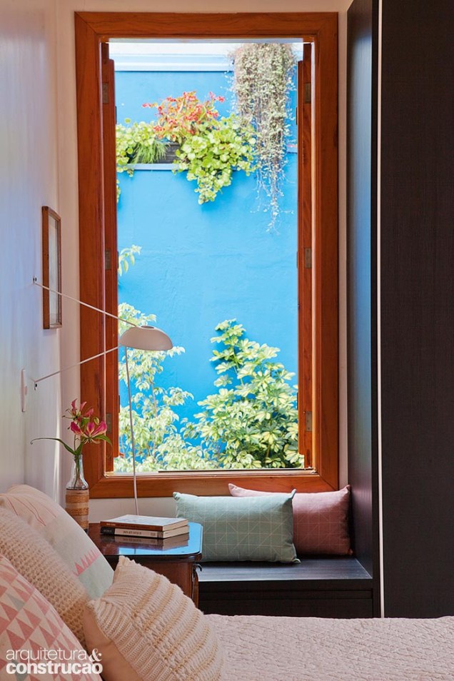 Ao lado da cama, a janela com banco de madeira (Luciano Santos) completa a vista para o verde e azul do jardim.
