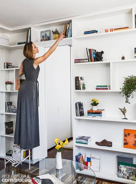 A estante acompanha todo o pé-direito de 2,50 m. Parte da decoração, a discreta escadinha ajuda a alcançar as prateleiras mais altas.