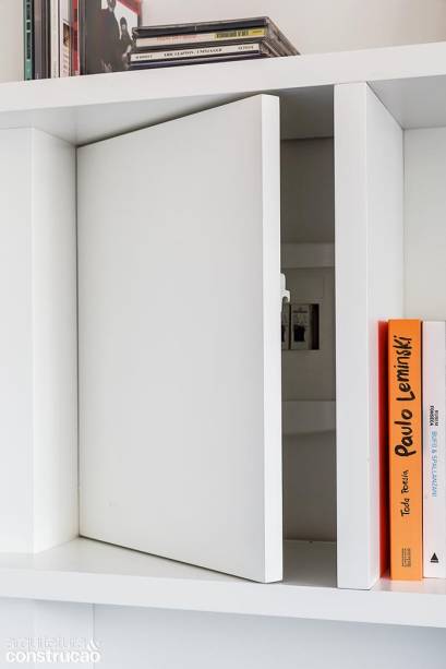 Como esconder o quadro de luz, situado na parede ao lado da porta de entrada, uma vez que a estante ocupa toda essa superfície? A solução foi instalar uma porta num dos módulos com ferragem de fecho-toque. Quando cerrada, ela desaparece camuflada no conjunto.