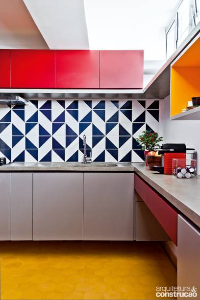 Depois de aberta e reposicionada na planta, a cozinha, visível da entrada, ganhou revestimento de azulejos (Lurca) e armários de laminado colorido da Formica: vermelho (ref. L 138 Vinho), cinza (ref. LN 80 Fendi) e mostarda (ref. L 523 Novo Cromo Real), mesmo tom do piso de ladrilho hidráulico hexagonal de 15 x 15 cm (Dalle Piagge).