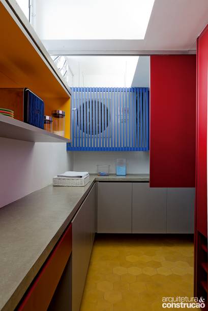 Observe o recorte do painel revestido de laminado vermelho, que corre num trilho preso no teto para esconder o ar-condicionado, disfarçado pelo módulo ripado azul.