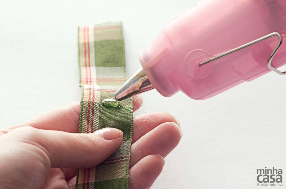 1. Meça a circunferência da vela e recorte uma faixa de tecido com 2 cm a mais do que essa medida. No centro, pingue uma gota de cola quente.