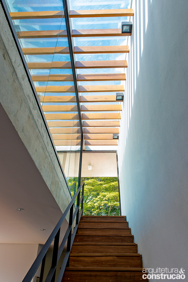 Sobre a escada que conduz ao terraço, o teto de vidro laminado é sustentado por pergolado com estrutura de alumínio e cumaru.