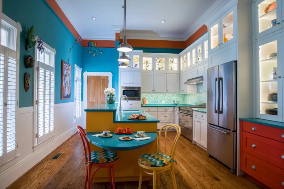 14-38-jeitos-de-incorporar-cor-na-sua-cozinha Cores dinâmicas e estampas vibrantes são uma combinação perfeita nesta cozinha de inspiração tropical da Copper Sky Renovations. As bancadas de superfície em turquesa adicionam um estilo colorido. Já as paredes azuis são coroadas por um corredor de teto laranja vibrante. O tecido chevron nas cadeiras confere um toque especial e um backsplash de mosaico de vidro multicolorido se destaca contra os gabinetes brancos.