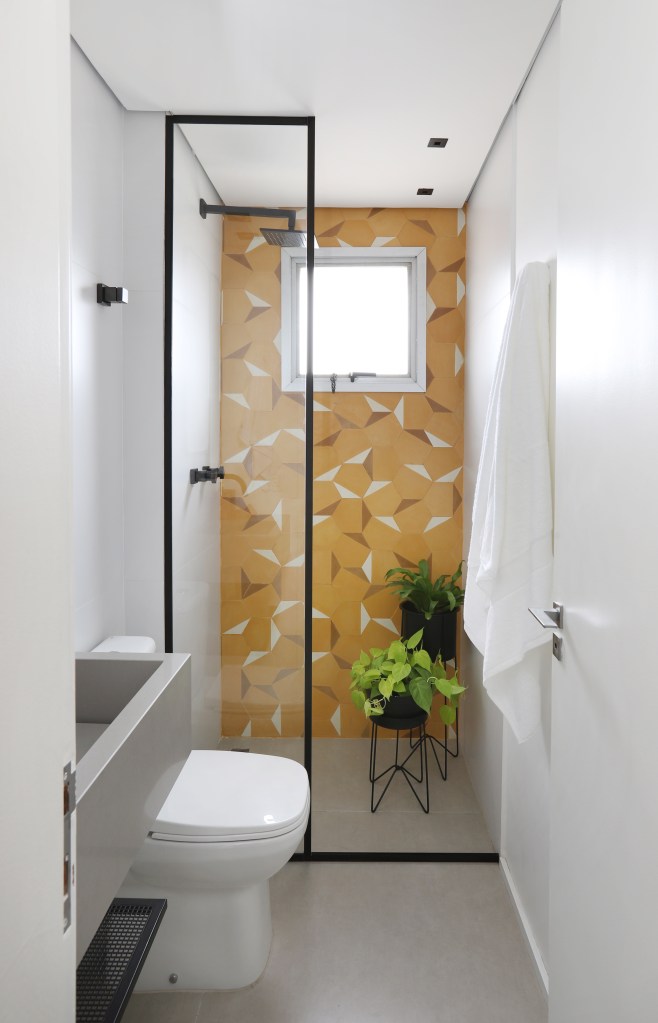 banheiro; piso de porcelanato; parede de ladrilhos amarelos; plantas; box de vidro
