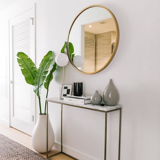 Hall com parede clara, espelho, e plantas decorativas.
