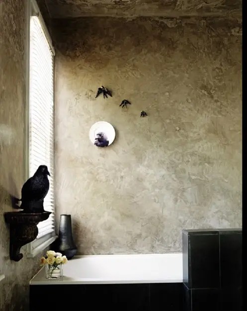 Um banheiro assombrado com decoração de pássaro, paredes de textura neutra, uma banheira preta e azulejos pretos.