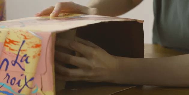 Mão colocando tubo de papel dentro de caixa