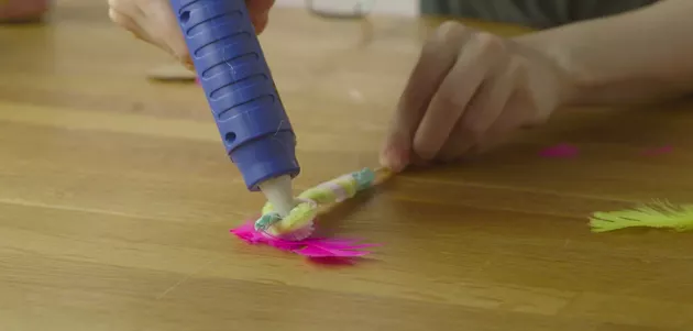 Mão grudando penas coloridas em graveto