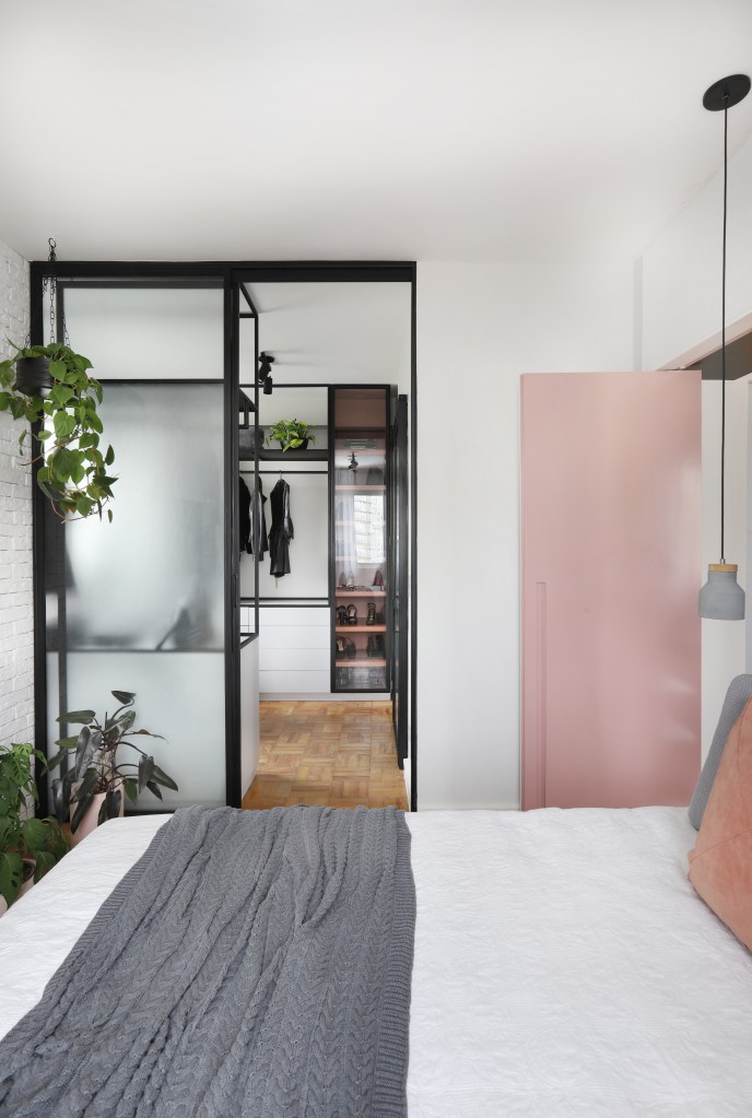Quarto com porta rosa, plantas penduradas e vista para closet.