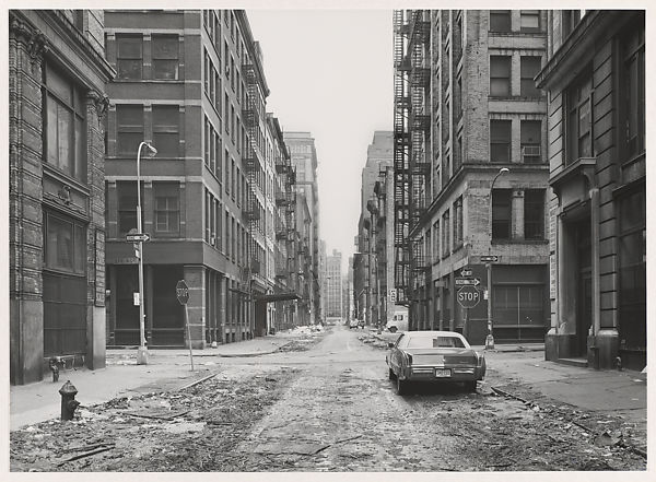 fotografia preta e branca de rua vazia com apenas um carro e prédios velhos