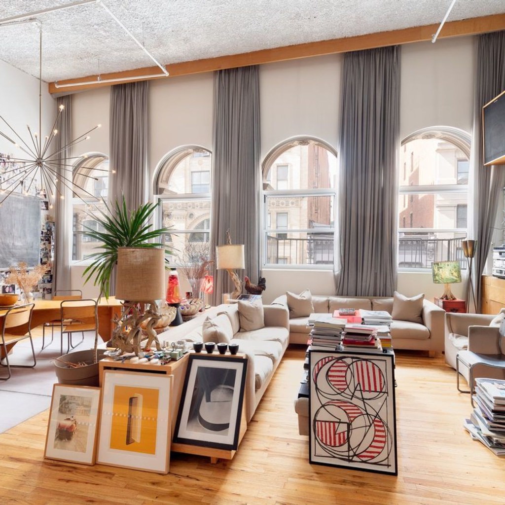loft com grandes janelas e sofá em formato L; quadros apoiados no chão e nos móveis