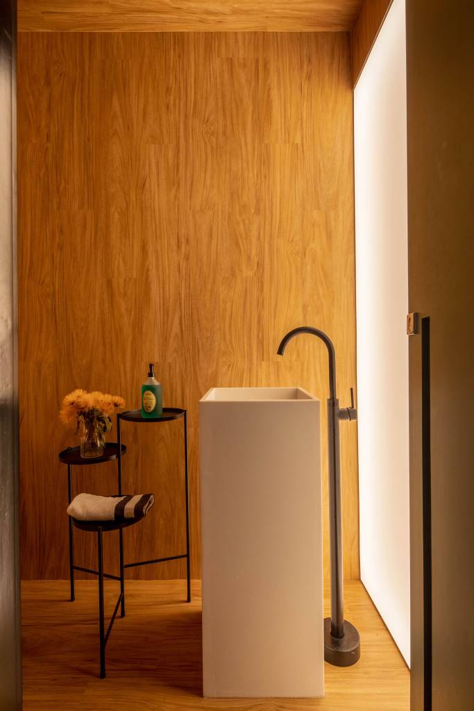 projeto-amplia-area-social-e-integrou-ambientes-em-ape-para-um-jovem-casal-casa.com-paprica-arquitetura-andre-nazareth-14-lavabo-cuba Lavabo com parede de madeira e cuba de chão branca, com torneira de chão e móvel em metal preto