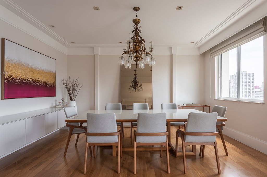 sala de jantar é composta pela mesa, em madeira e laca branca, e cadeiras também em madeira e linho cinza claro, projeto por Gabriela Casagrande Arquitetura