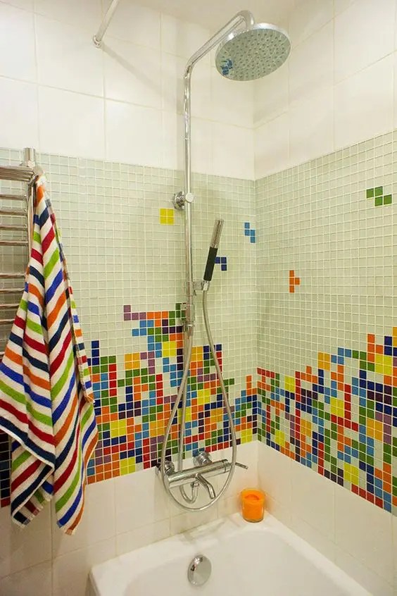 Banheiro com uma mistura de azulejos brancos de grande escala, verdes de pequena escala e um mosaico de pequenas peças coloridas