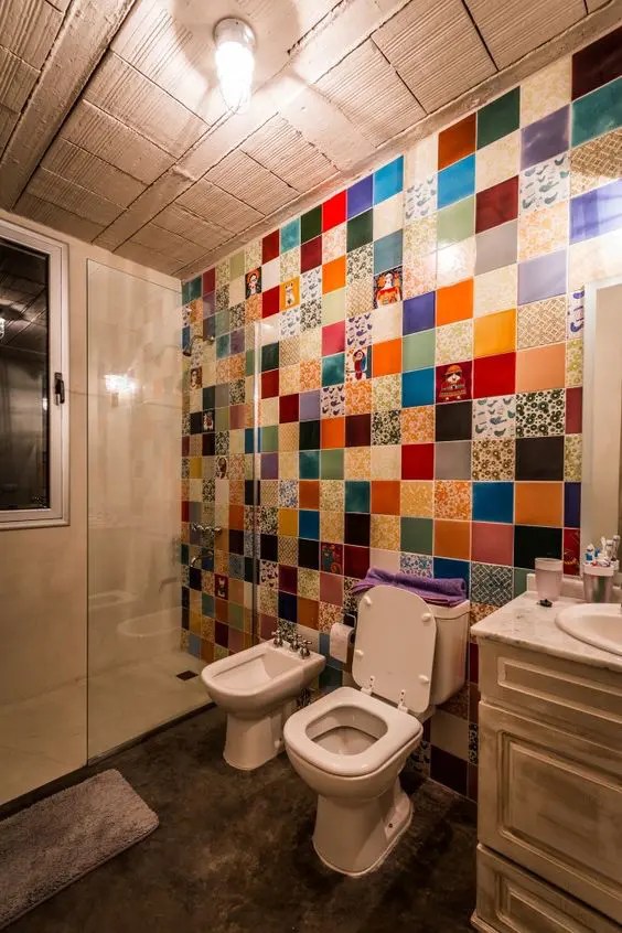 Um banheiro brilhante com uma parede revestida de azulejos coloridos, piso de concreto e uma penteadeira chique