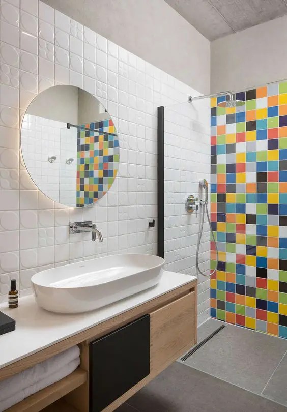 Banheiro neutro com azulejos brancos nas paredes, cinzas de grande escala no chão e uma parede multicolorida