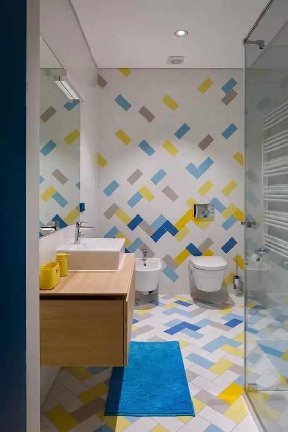 Azulejos com tons de azul, amarelo e cinza, com um tapete combinando e uma pia flutuante