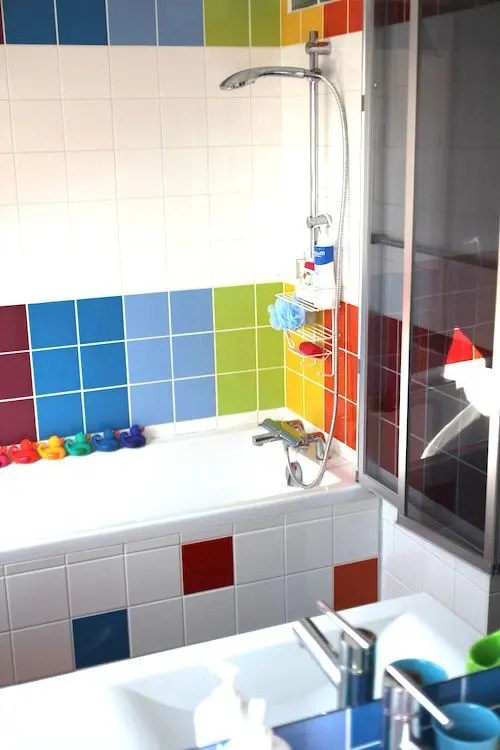 Banheiro moderno com azulejos super brilhantes em todas as cores do arco-íris e pequenos patos de brinquedos repetindo essas cores