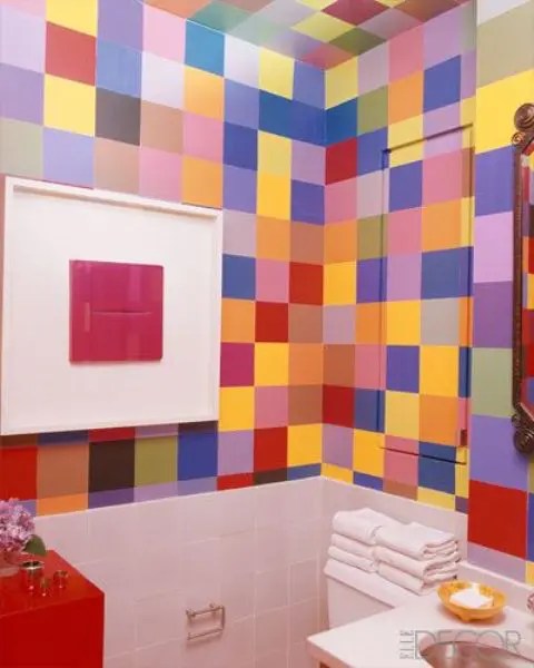 Um pequeno lavabo colorido com azulejos chamativos por toda parte, um armário vermelho e uma obra de arte ousada