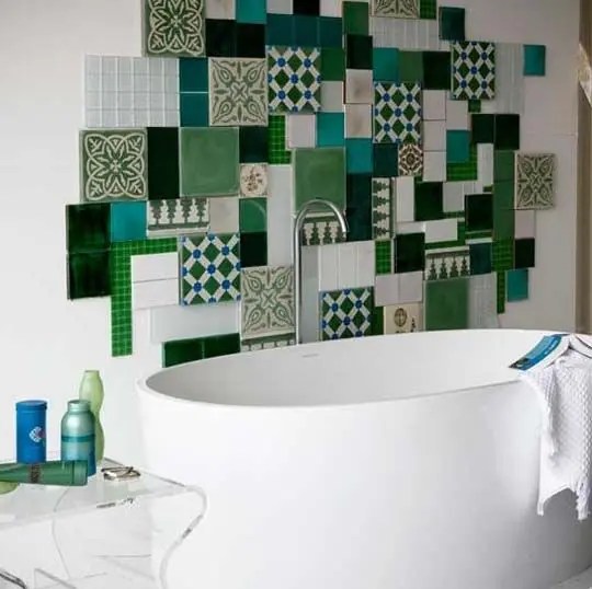Uma parede reúne diferentes azulejos verde e azuis estampados e parece uma obra de arte