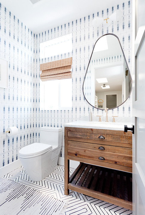 Banheiro com papel de parede preto e branco, armário de madeira e espelho oval