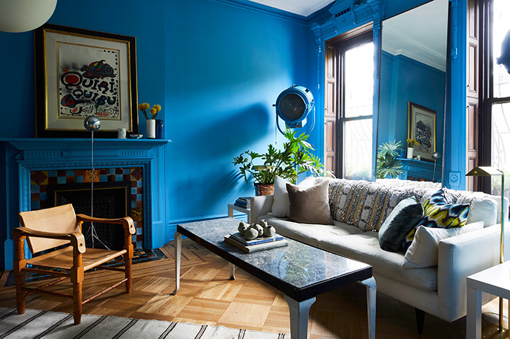 Sala de estar com paredes azuis, sofá cinza, mesa central, poltrona de madeira e uma lareira