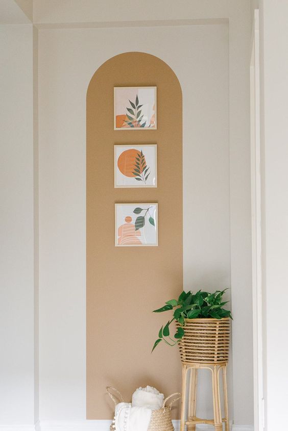 Arco neutro em uma parede branca com 3 quadros e uma planta posicionada no chão