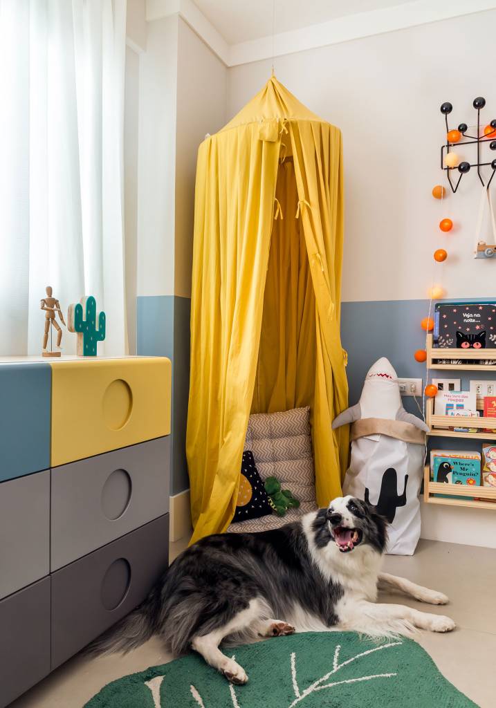 Cômoda nas cores cinza escuro, cinza claro, azul e amarelo e cabana com dossel amarelo, com cachorro deitado na frente