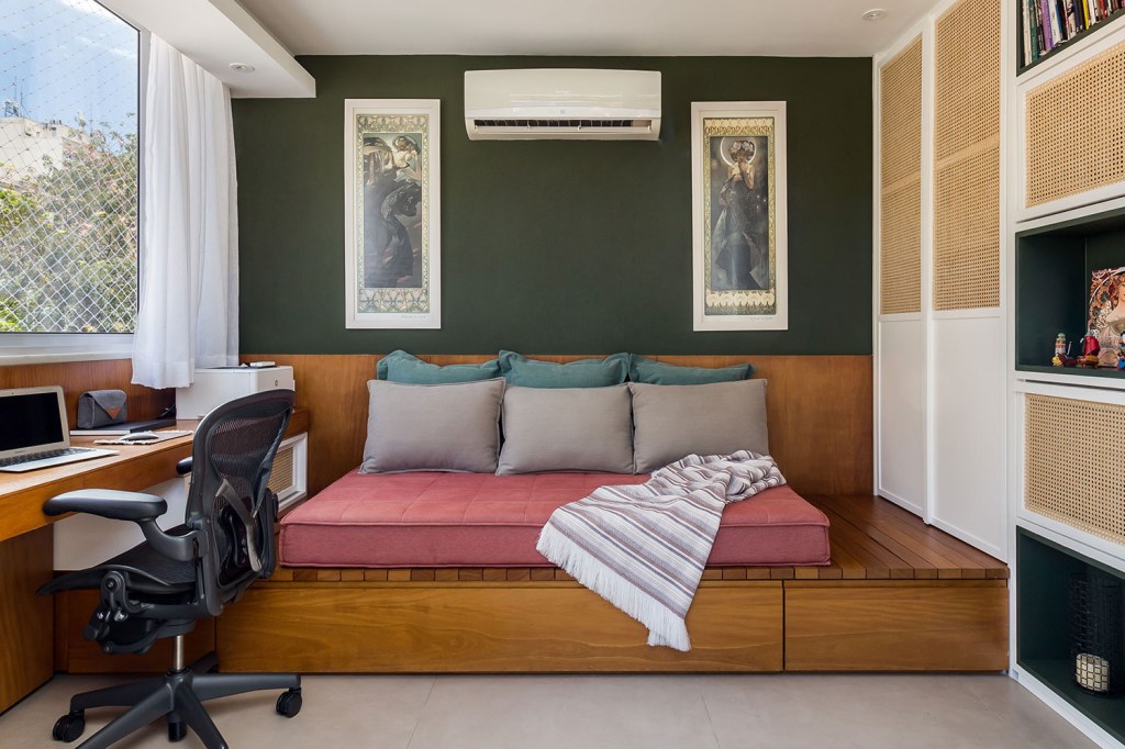 Sofá cama com colchão rosa, e almofadas verde e conza. Parede verde com dois quadros