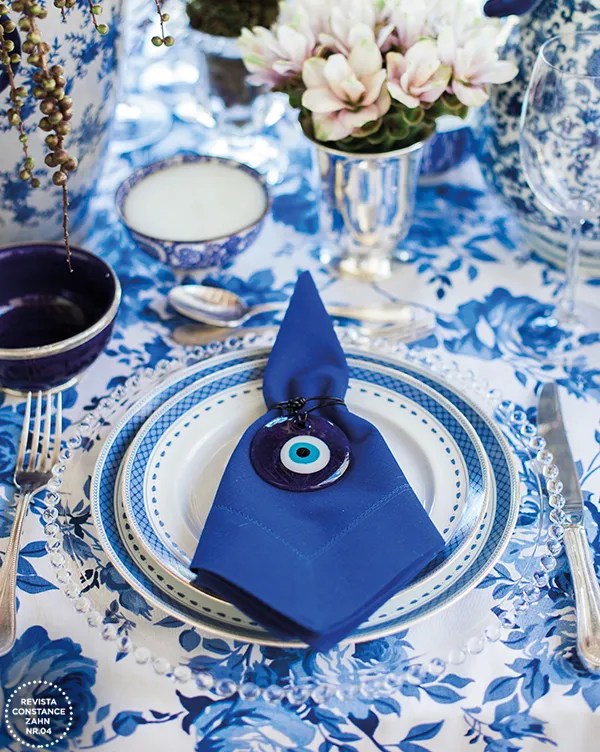 Mesa de jantar com guardanapo e pratos azuis e enfeite com olho grego