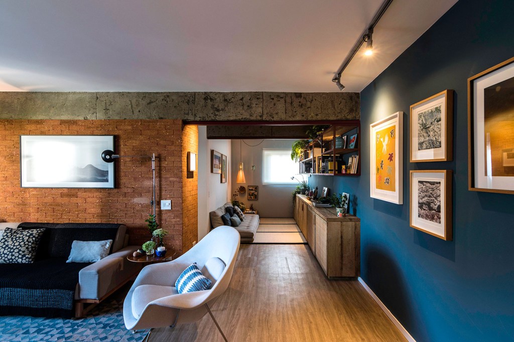 Sala de estar integrada, com piso de madeira, parede azul e de tijolinhos