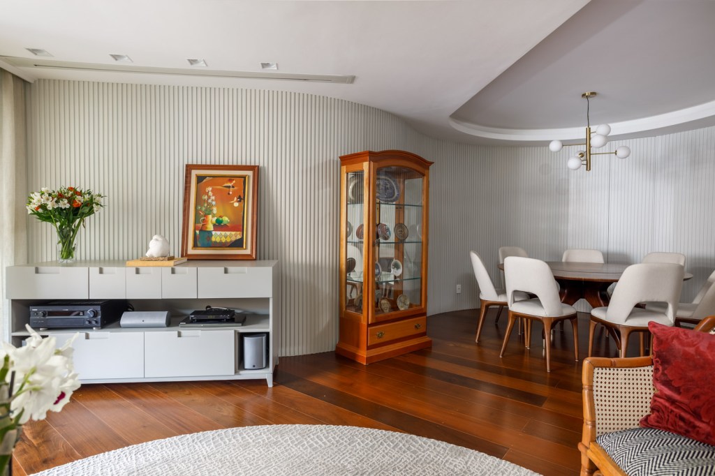 Ampla sala integrada com sala de jantar, um grande aparador branco e uma cristaleira de madeira.
