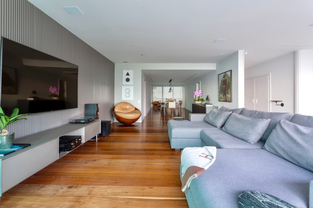 Sala de estar integrada com piso de madeira e sofá grande cinza