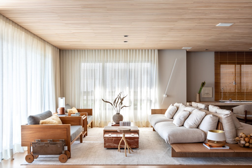 Sala de estar com ripas de madeira clara no teto e décor neutro