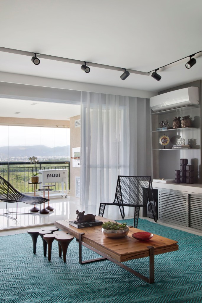 Varanda integrada à sala de estar com tapete turquesa e mesa de centro de madeira