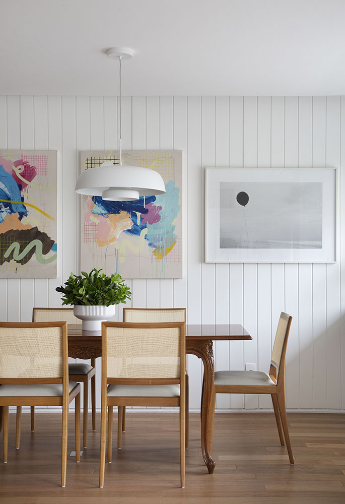 Sala de jantar com parede em madeira branca e três quadros