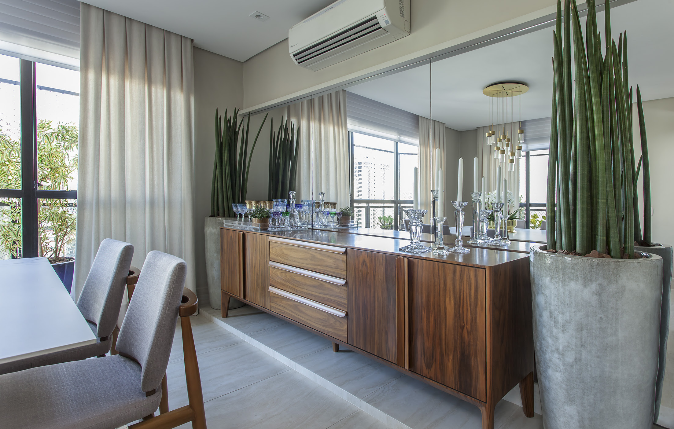Buffets-da-sala-e-jantar-dicas-de-como-escolher-08 Este buffet em madeira Nogueira acompanha a parede espelhada e é ladeado por vasos cerâmicos com lanças de São Jorge. Além de sua função de guardar louças, revela um décor de personalidade na sala de jantar dos moradores