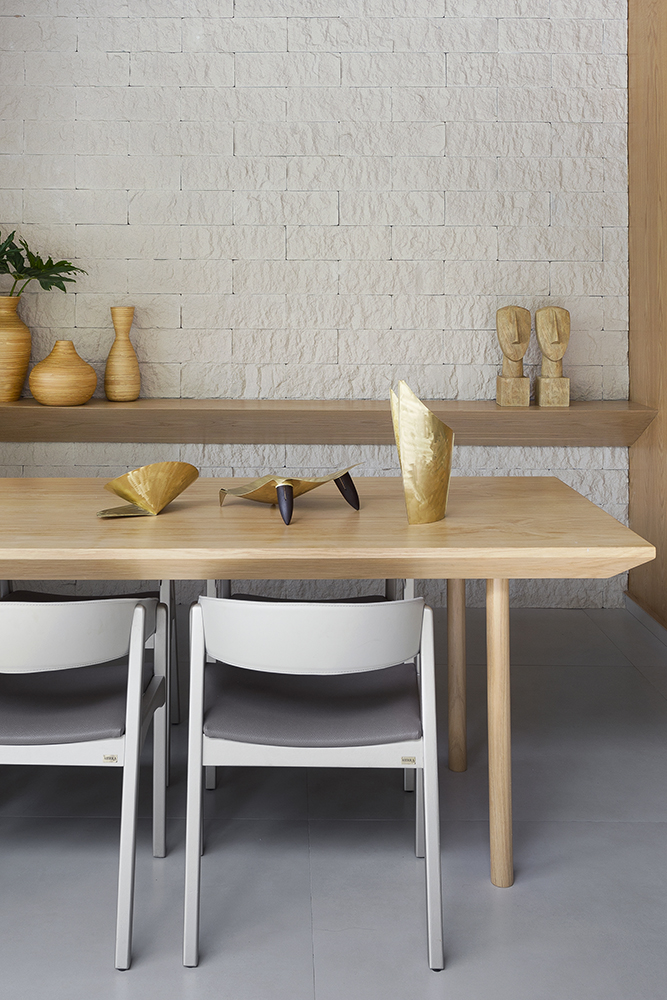 Sala de jantar com mesa em madeira; prateleiras com vasos ao fundo