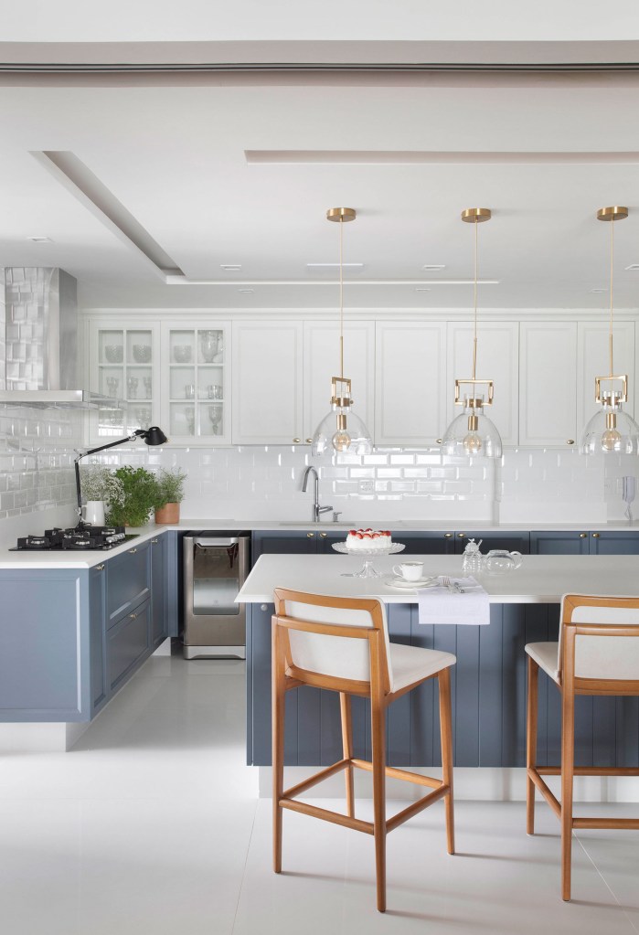 Cozinha com móveis inferiores em azul e aéreos branco, coms puxadores dourados e ilha no meio do cômodo