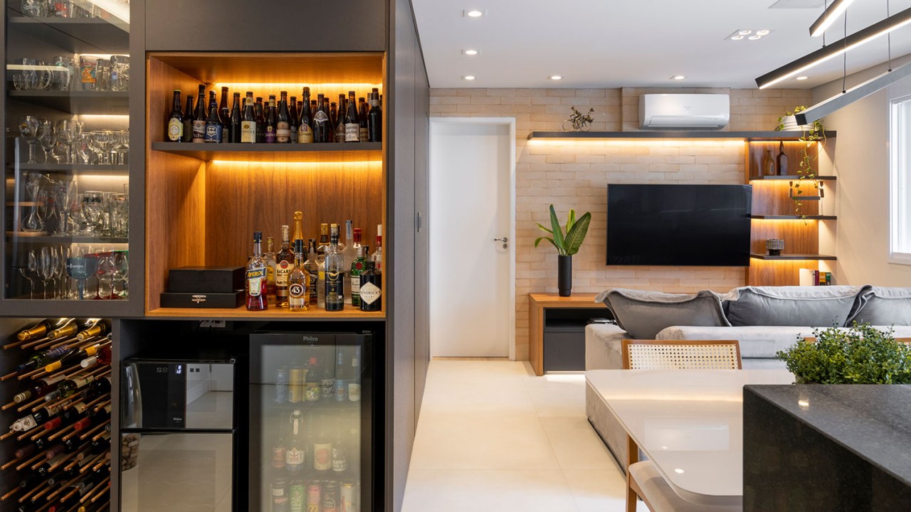 Apartamento com sala integrada ampla mobiliário em preto, madeira e branco. Com um bar cheio de garrafas e adega
