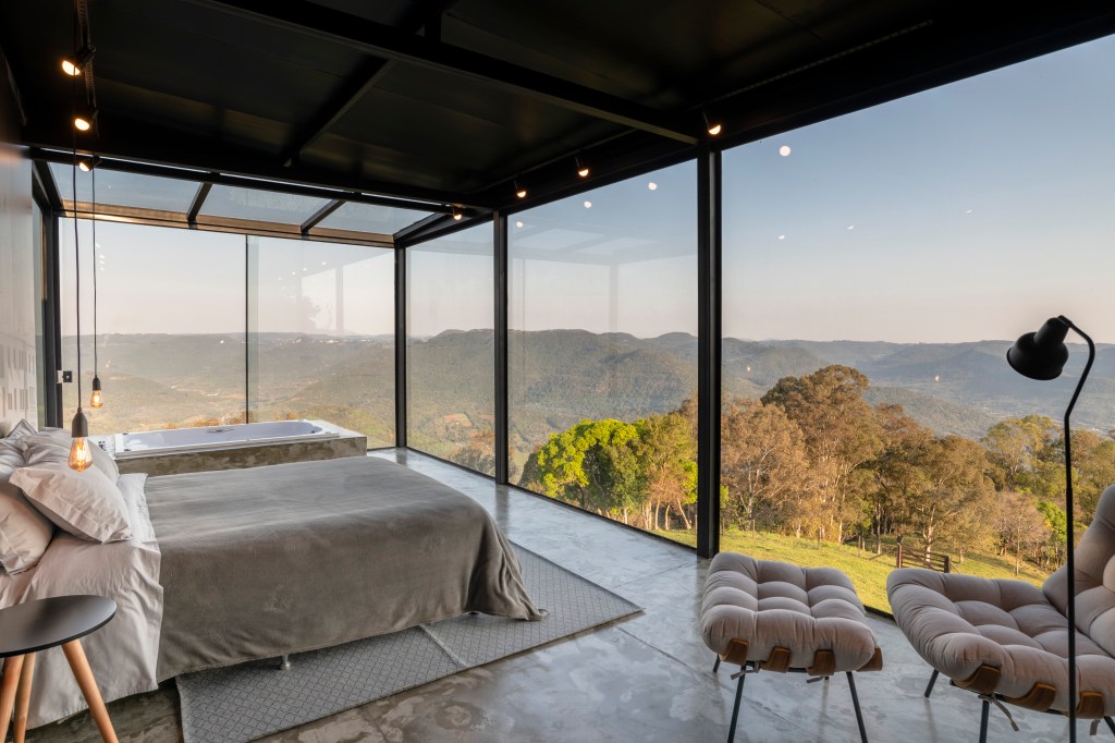 Quarto com banheira em cabana na montanha com paredes de vidro e vista panorâmica para a paisagem.