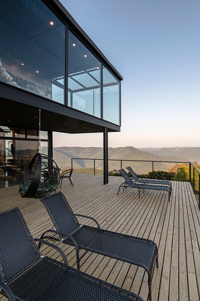 Deck de casa na montanha com vista panorâmica para paisagem natural deslumbrante e andar superior com panos de vidro.