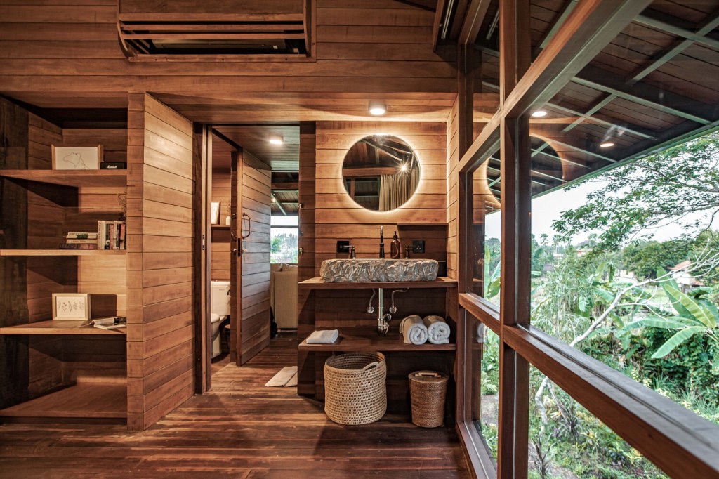 Banheiro com bancada de pia e espelho em madeira, com cabine ao fundo em estrutura totalmente de madeira.