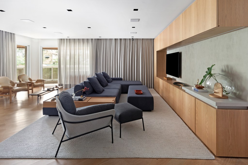 Sala de estar integrada com painel de madeira, sofá azul marinho e detalhes cinza