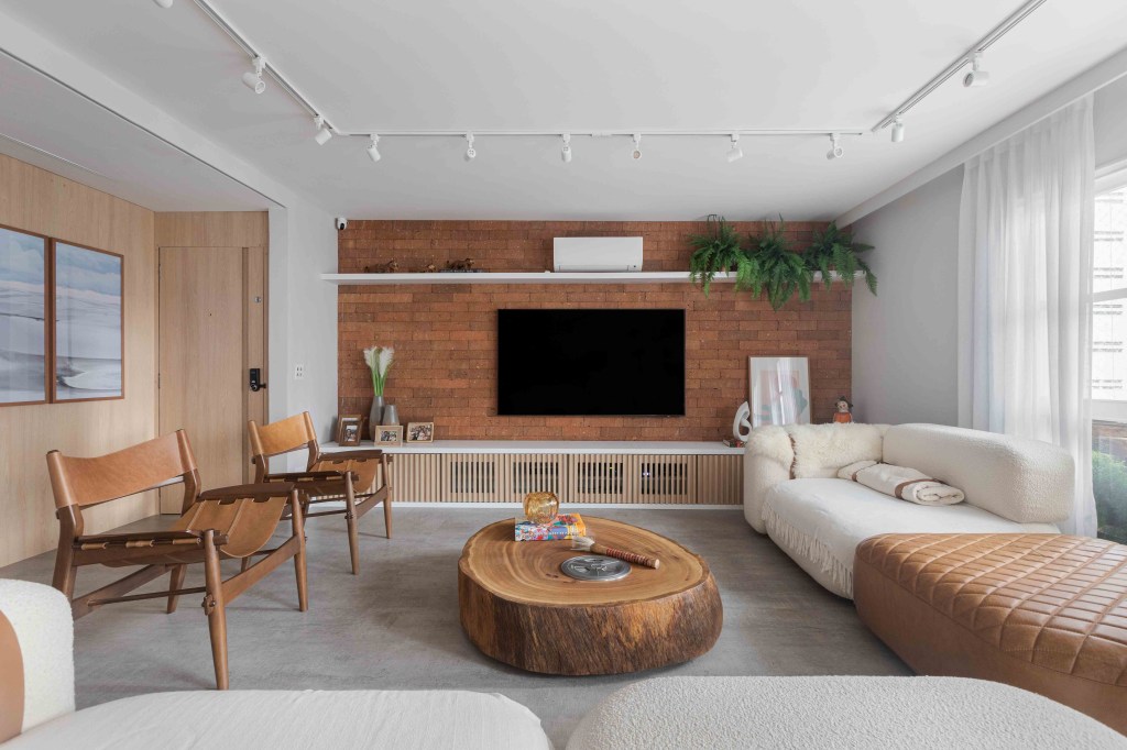 Sala de estar com painel de tijolinhos marrons, sofá branco e mesa de centro de tronco de madeira