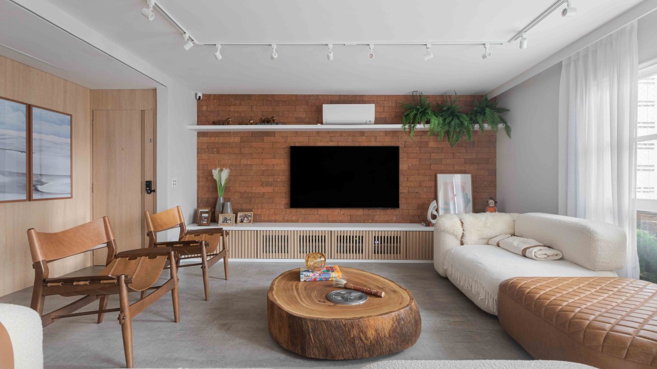 Sala de estar com painel de tijolinhos marrons, sofá branco e mesa de centro de tronco de madeira
