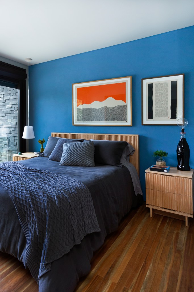 Quarto de casal com parede azul, quadro laranja e piso de madeira