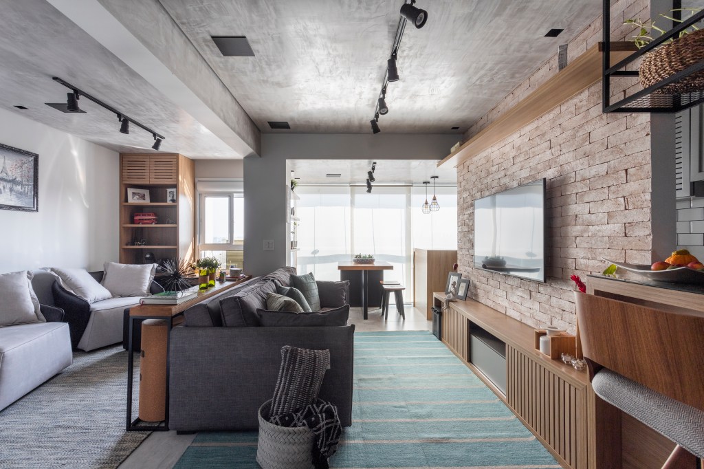 Sala de estar integrada com tijolinhos, sofá cinza, tapete verde e cimento queimado